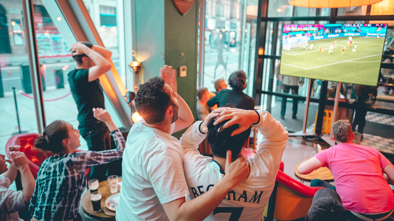 A group of people excitedly watching a football match at Ludo sports bar