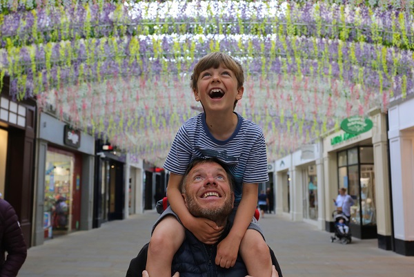 Son sat on father's shoulders with father looking up and smiling