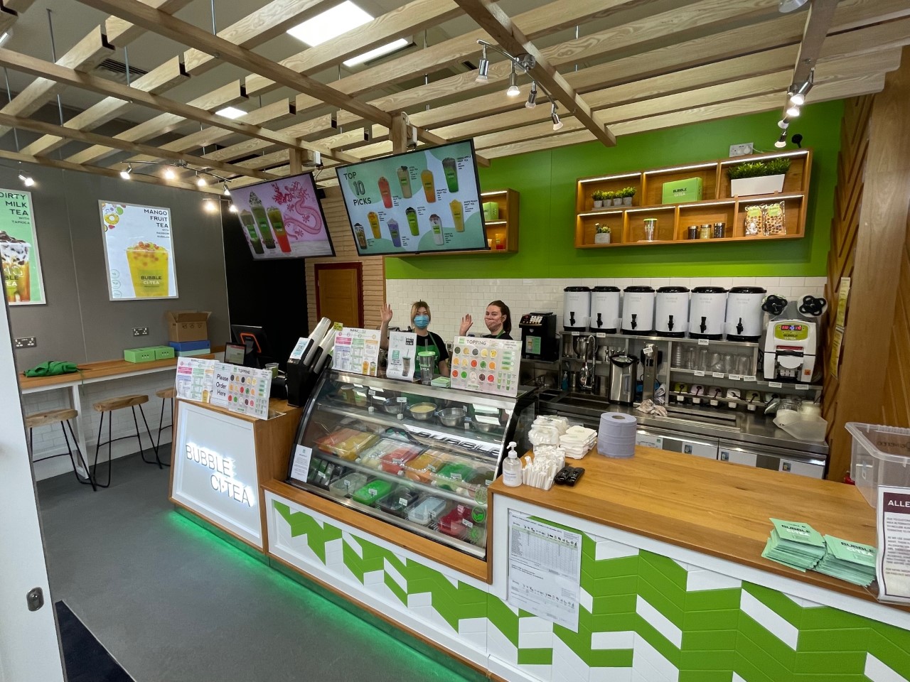 The interior of Bubble CiTea at Southgate Bath, with two people waving from behind the counter.